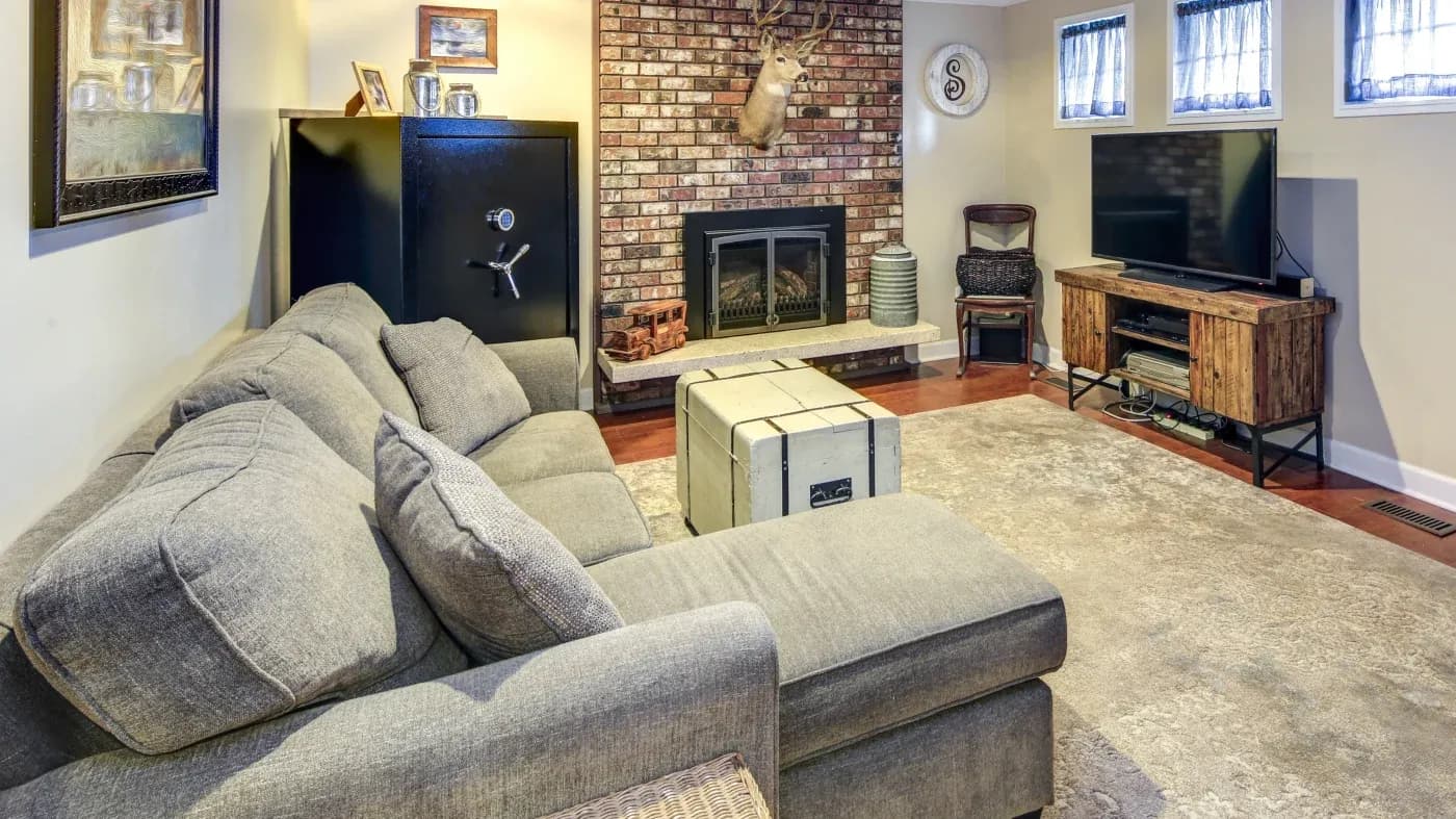 Cozy living room with gray sectional sofa, brick fireplace with mounted deer head, flat-screen TV on a wooden stand, and a crate-style coffee table.