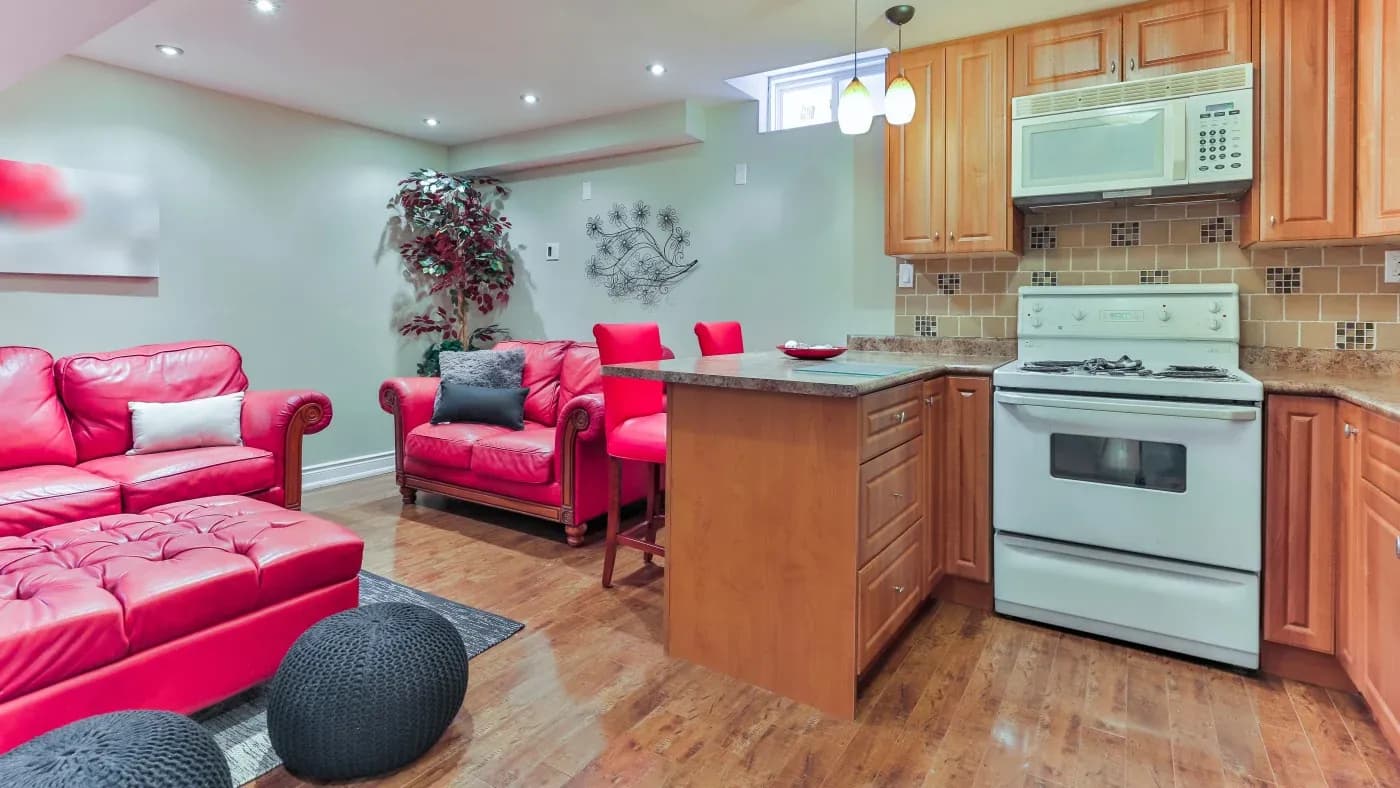 Cozy living room and kitchen combo with vibrant red sofas and chairs, wood cabinets, white appliances, and a decorative plant, creating a warm, inviting atmosphere.