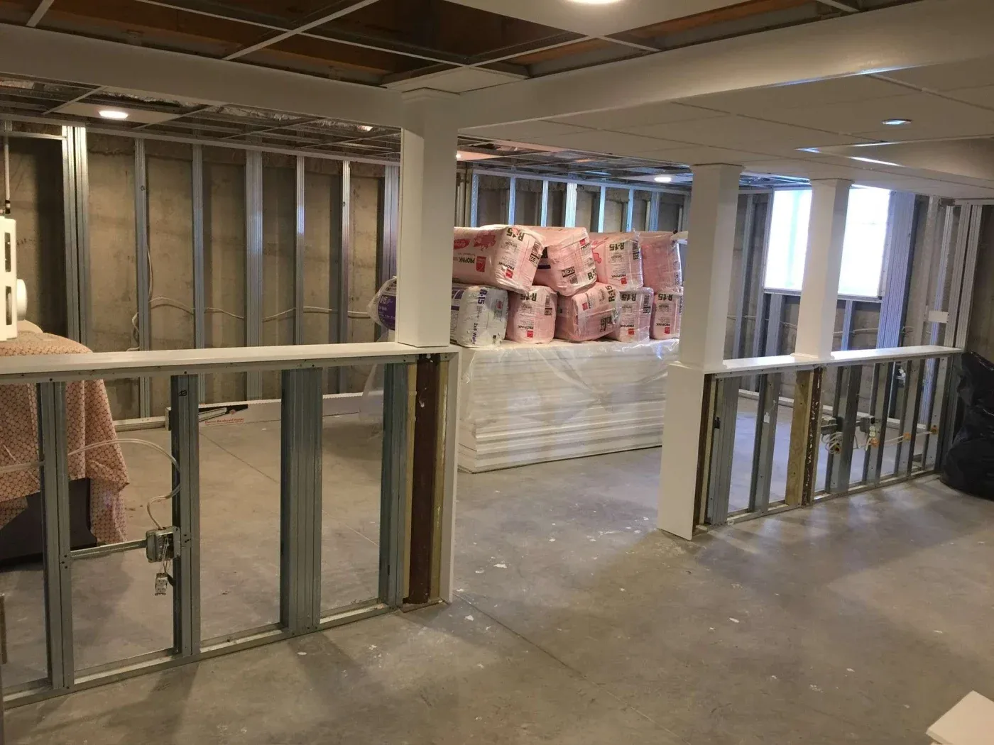 Partially finished basement with exposed frame walls, piled insulation, and ceiling grid. A light and organized layout ready for further renovation.