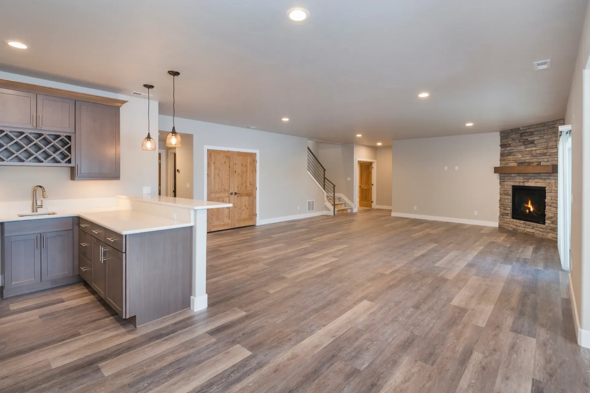 Spacious open-concept room with wood floors, a modern kitchen with gray cabinets on the left, and a stone fireplace on the right. Warm, inviting ambiance.
