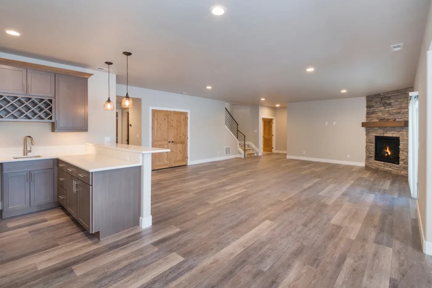 Spacious open-plan room with wood flooring, modern kitchen, and an inviting stone fireplace. Warm lighting creates a cozy, welcoming atmosphere.