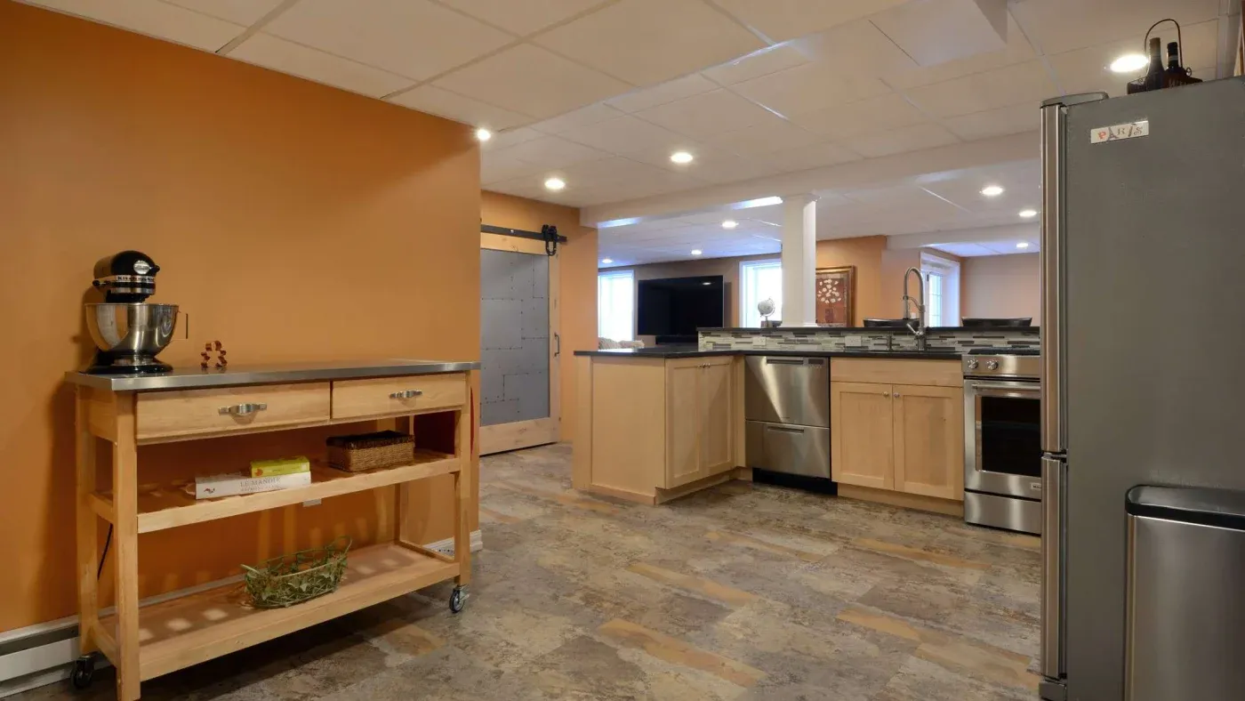 Spacious kitchen with warm orange walls, featuring stainless steel appliances, wooden cabinetry, a rolling cart with a mixer, and tile flooring. Cozy and modern.