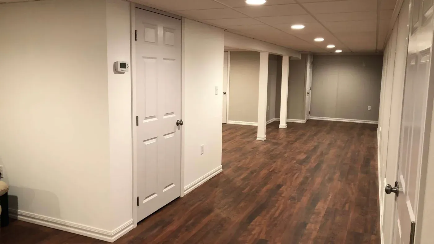 Finished basement with white walls, recessed lighting, and wood-style flooring. The space looks spacious and modern, with doors lining one side.