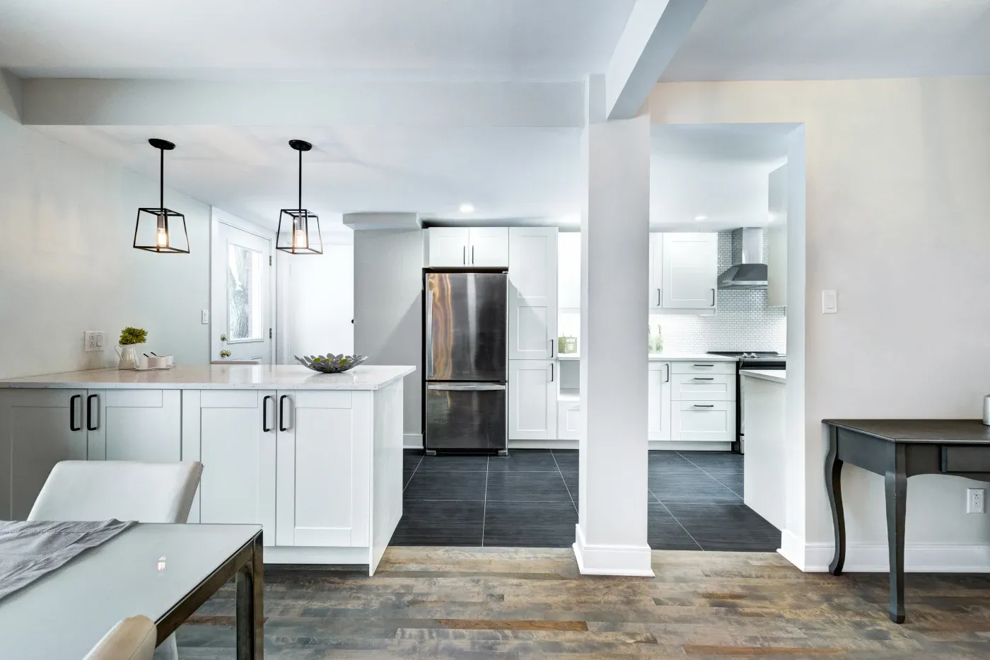 Modern kitchen with white cabinets, stainless steel appliances, and dark tile floors. Pendant lights hang over an island, creating a sleek, inviting space.