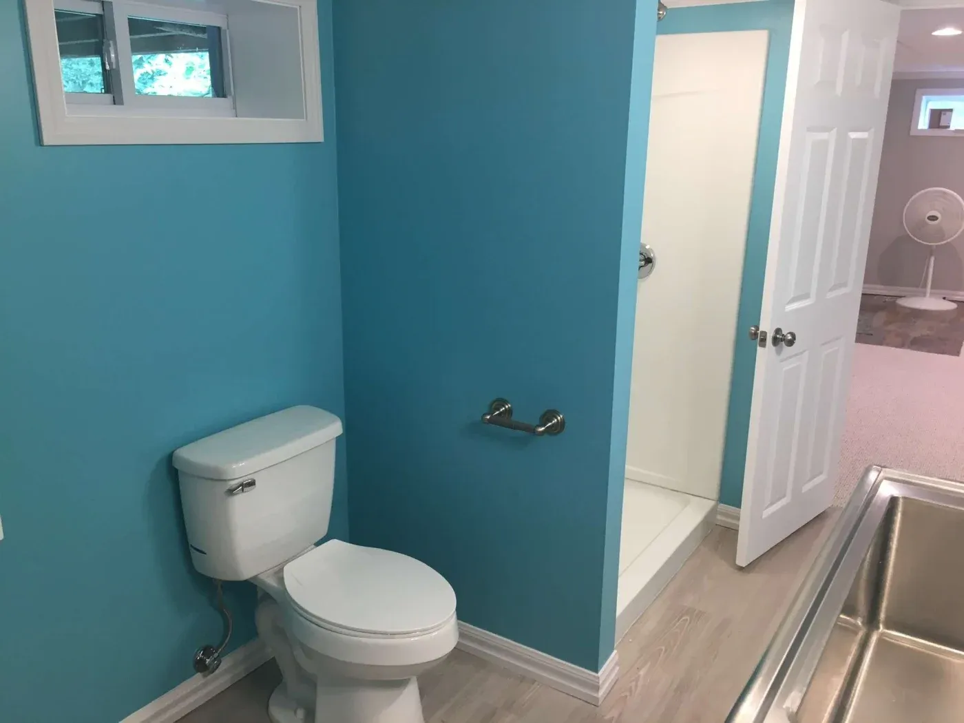 A bathroom with bright blue walls features a white toilet and a shower with a partially open door. The atmosphere is clean and modern.