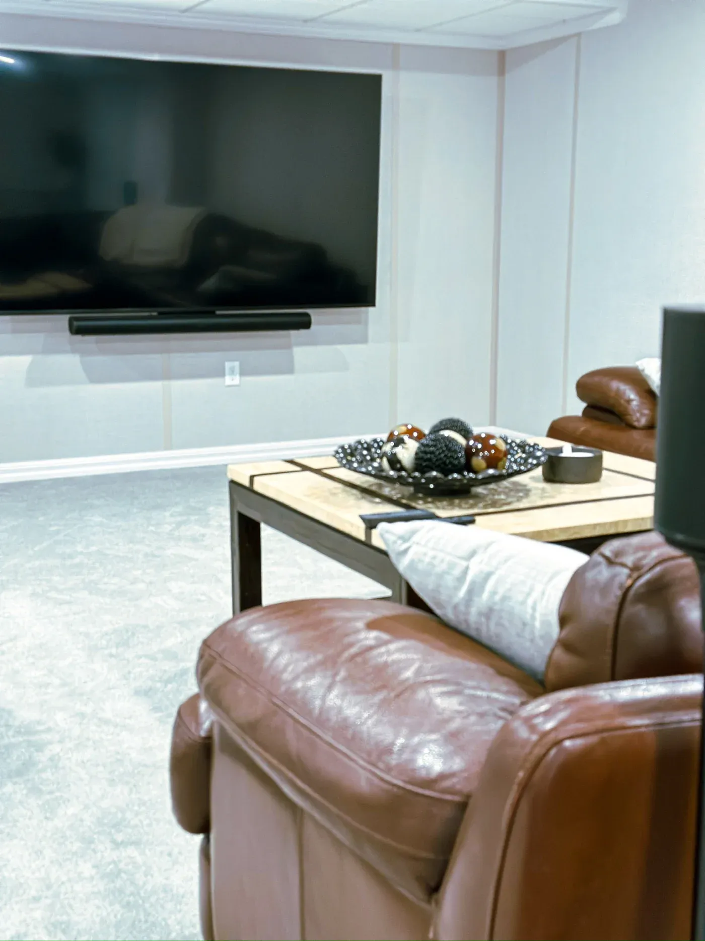 Cozy living room with brown leather couches, a large wall-mounted TV, and a wooden coffee table. Decorative bowls with orbs add elegance.