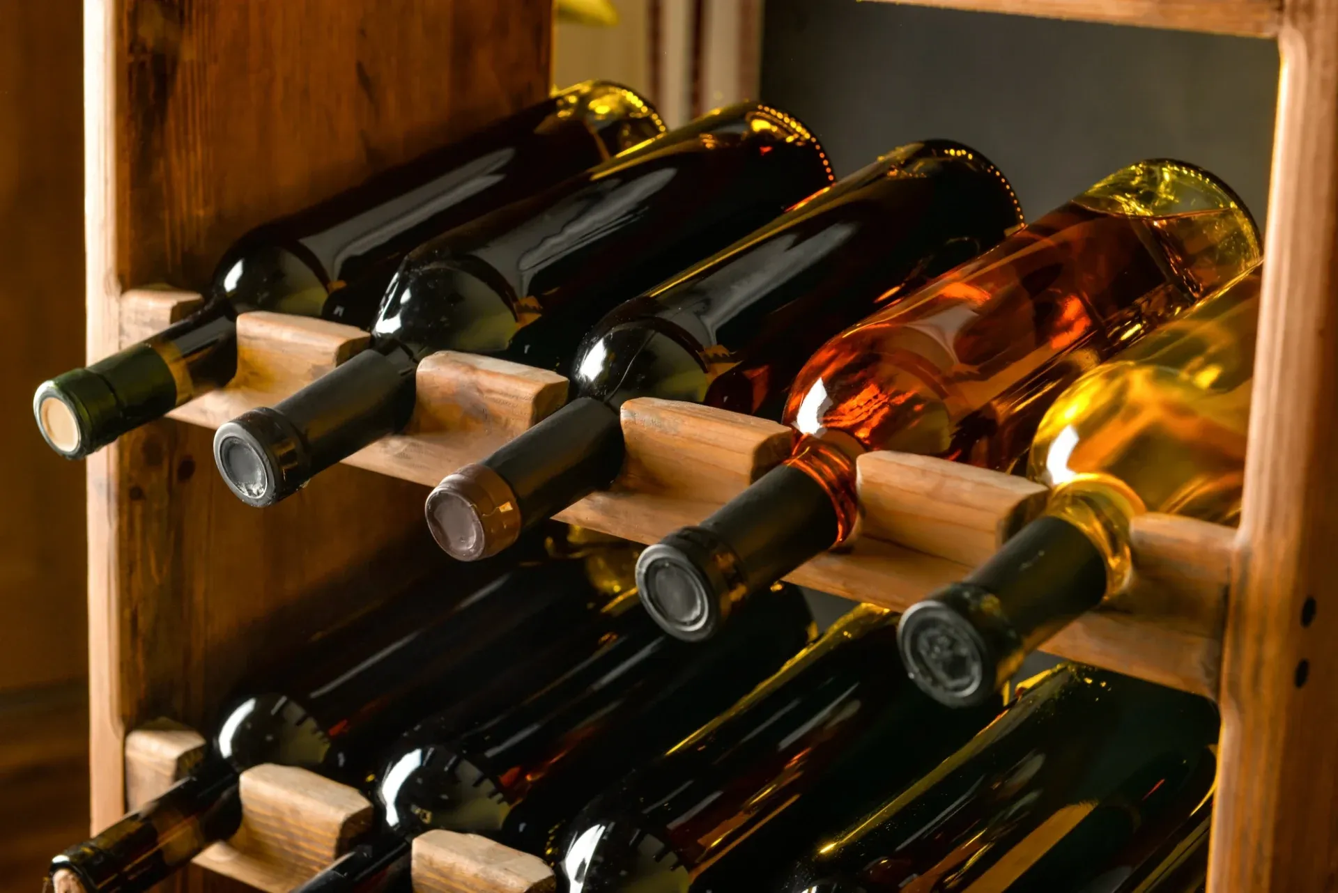Wooden wine rack holding an assortment of red, white, and rose wine bottles. The warm lighting creates an inviting and sophisticated ambiance.