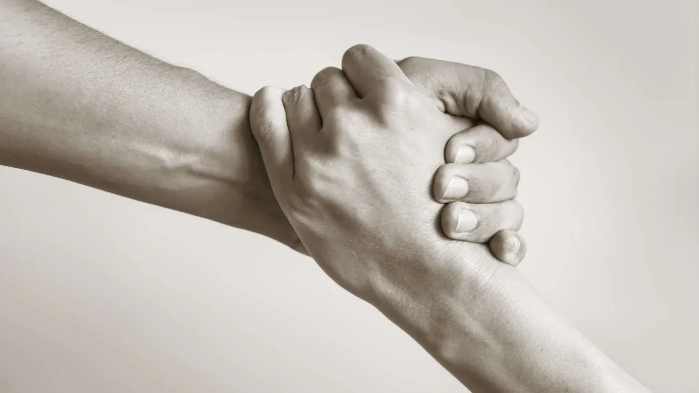 Two hands interlocked, symbolizing support and unity. One hand grips the wrist of the other, conveying strength and trust in a neutral tone.