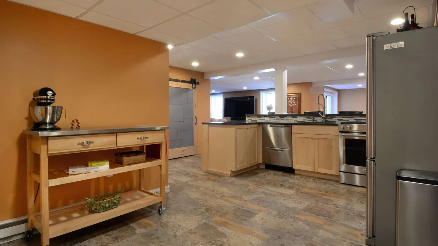 Spacious kitchen with warm, orange walls and modern appliances. Features a rolling wooden cart, stainless steel stove, and a gray barn-style door. Cozy ambiance.