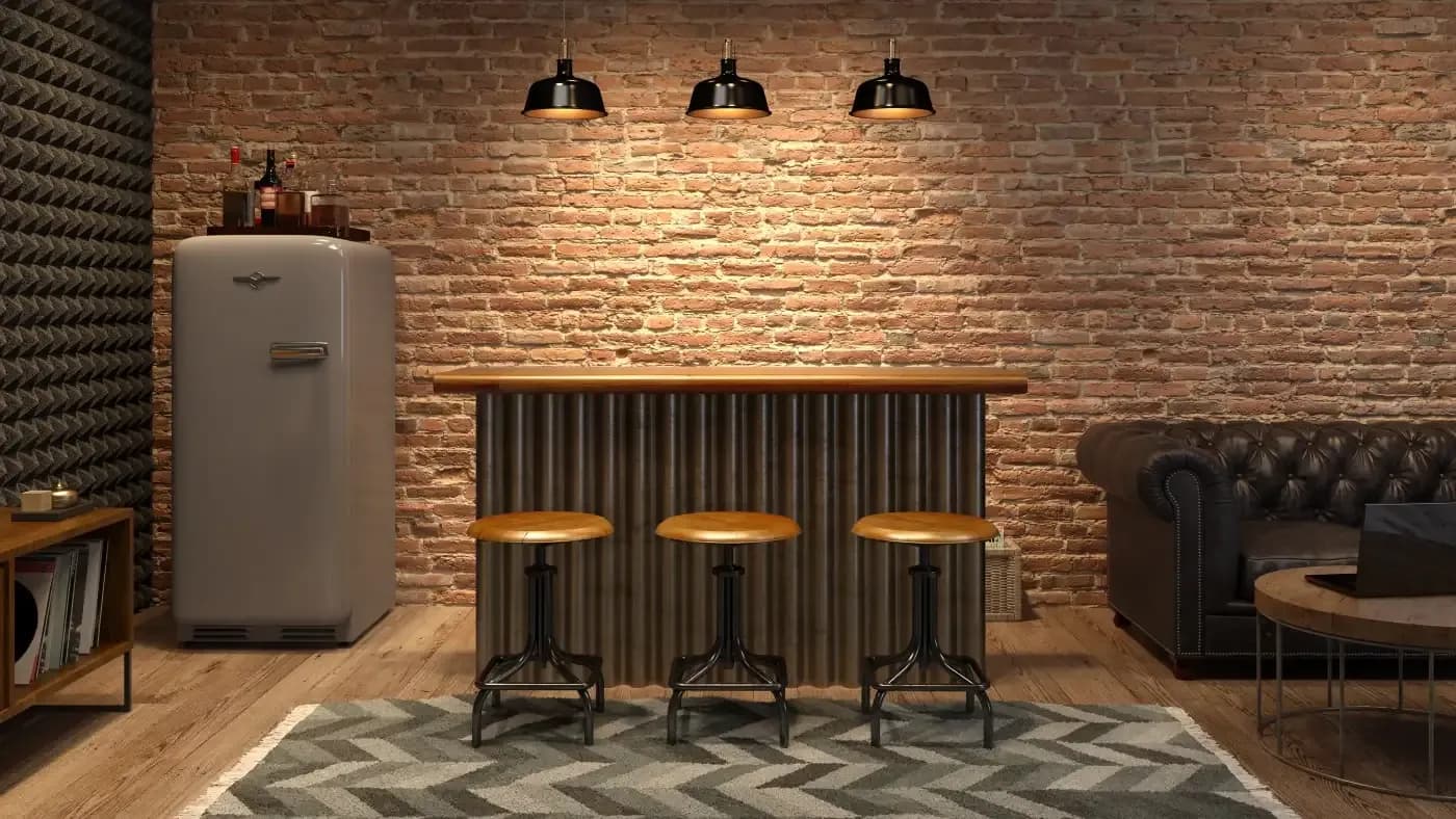 A cozy loft-style room with a brick wall, vintage fridge, and wooden bar counter. Three stools line the bar, under warm overhead lights, next to a leather sofa.