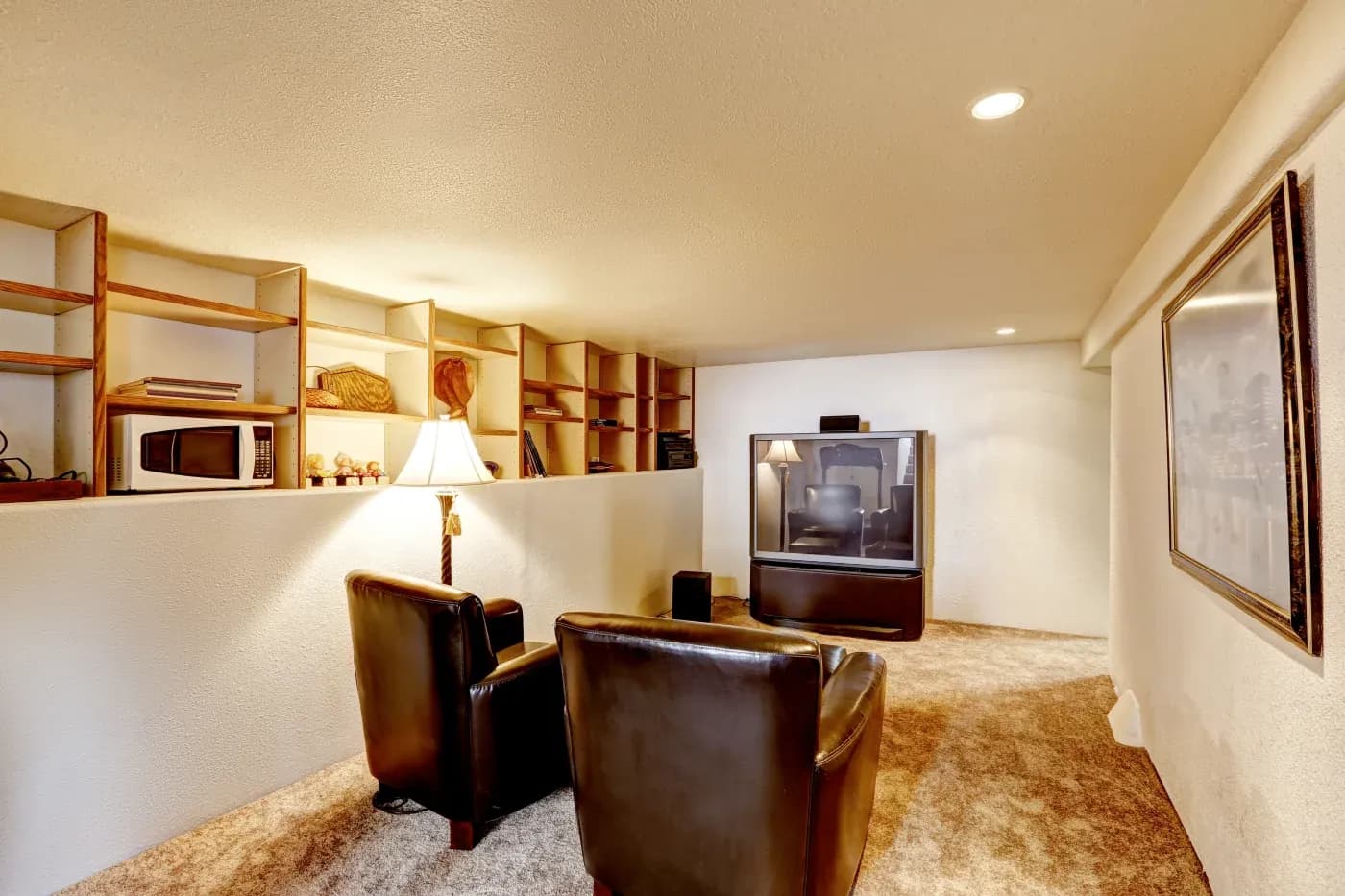 Cozy room with two black leather chairs facing an old-style TV. Shelves line the wall with a microwave and decor. Warm lighting creates an inviting atmosphere.