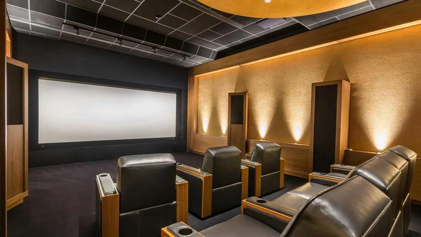 Luxurious home theater with six black leather recliners, soft lighting on textured beige walls, and a large screen, creating an inviting atmosphere.