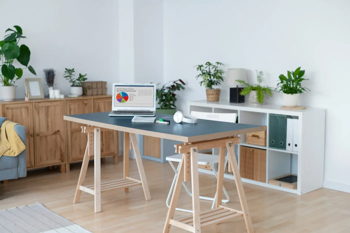 Modern home office with a minimalist desk, laptop displaying a chart, and chair. Wooden shelves and houseplants create a calm, organized atmosphere.