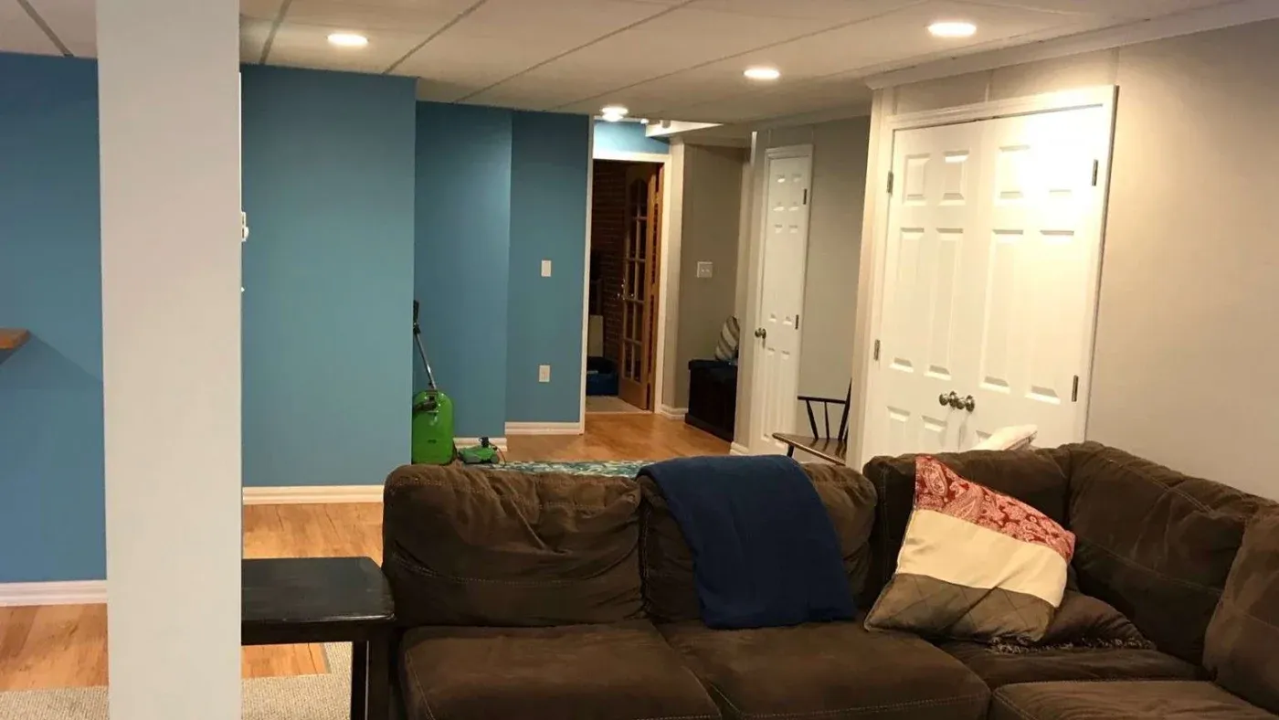 A cozy basement living area with blue and white walls. A brown sectional sofa with cushions is in the center, creating a warm, inviting atmosphere.