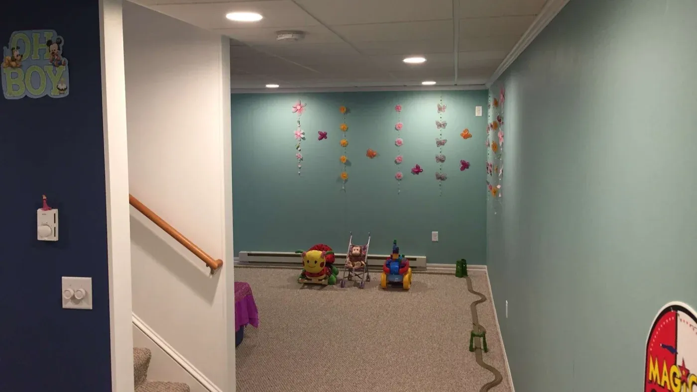 Basement playroom with teal walls decorated with colorful butterflies. Toys, including an activity center and toy stroller, are on the carpeted floor. Warm, inviting atmosphere.