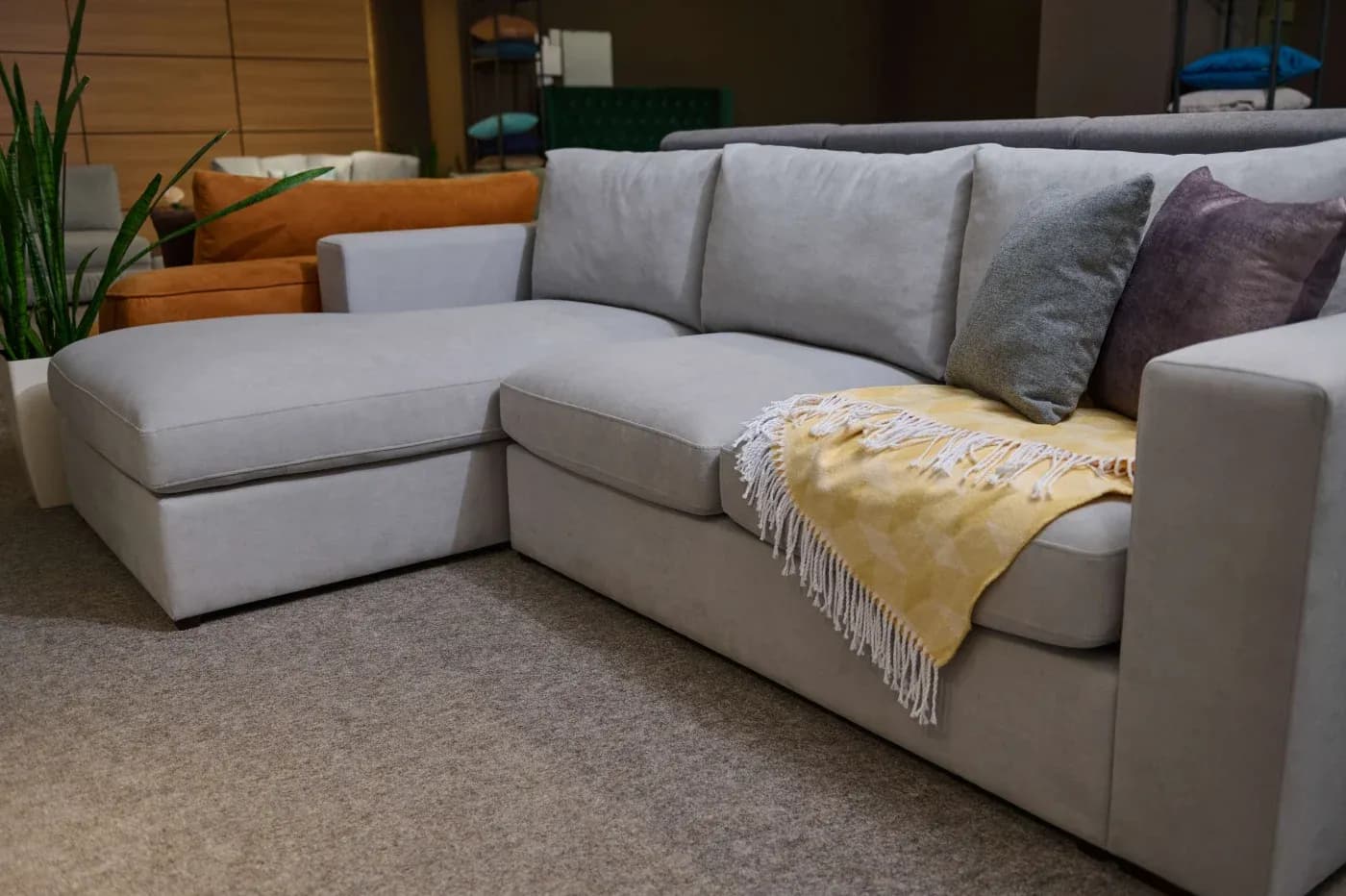 Spacious living room with a light gray sectional sofa, adorned with a yellow fringed throw and colorful pillows, surrounded by cozy decor.