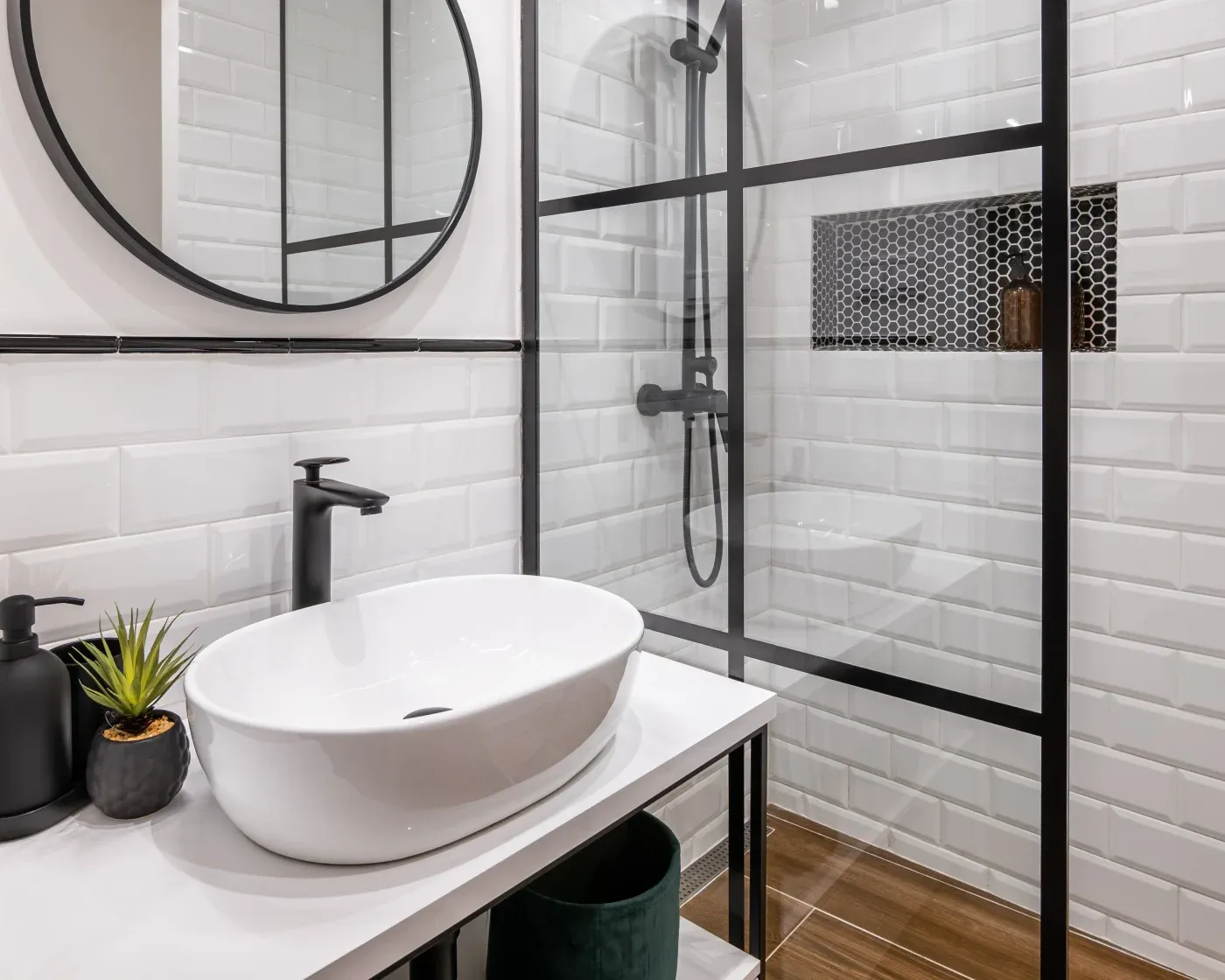 Modern bathroom with white subway tiles, a circular mirror above a sleek sink, and a black-framed glass shower. Minimalist and clean design.