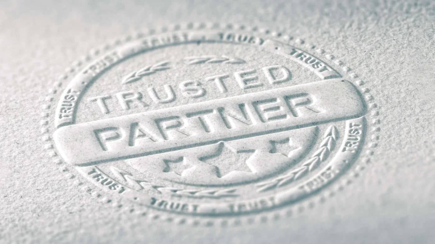 Embossed seal on paper reads "Trusted Partner" with stars and laurel. Words "Trust" encircle the seal. Conveys reliability and professionalism.