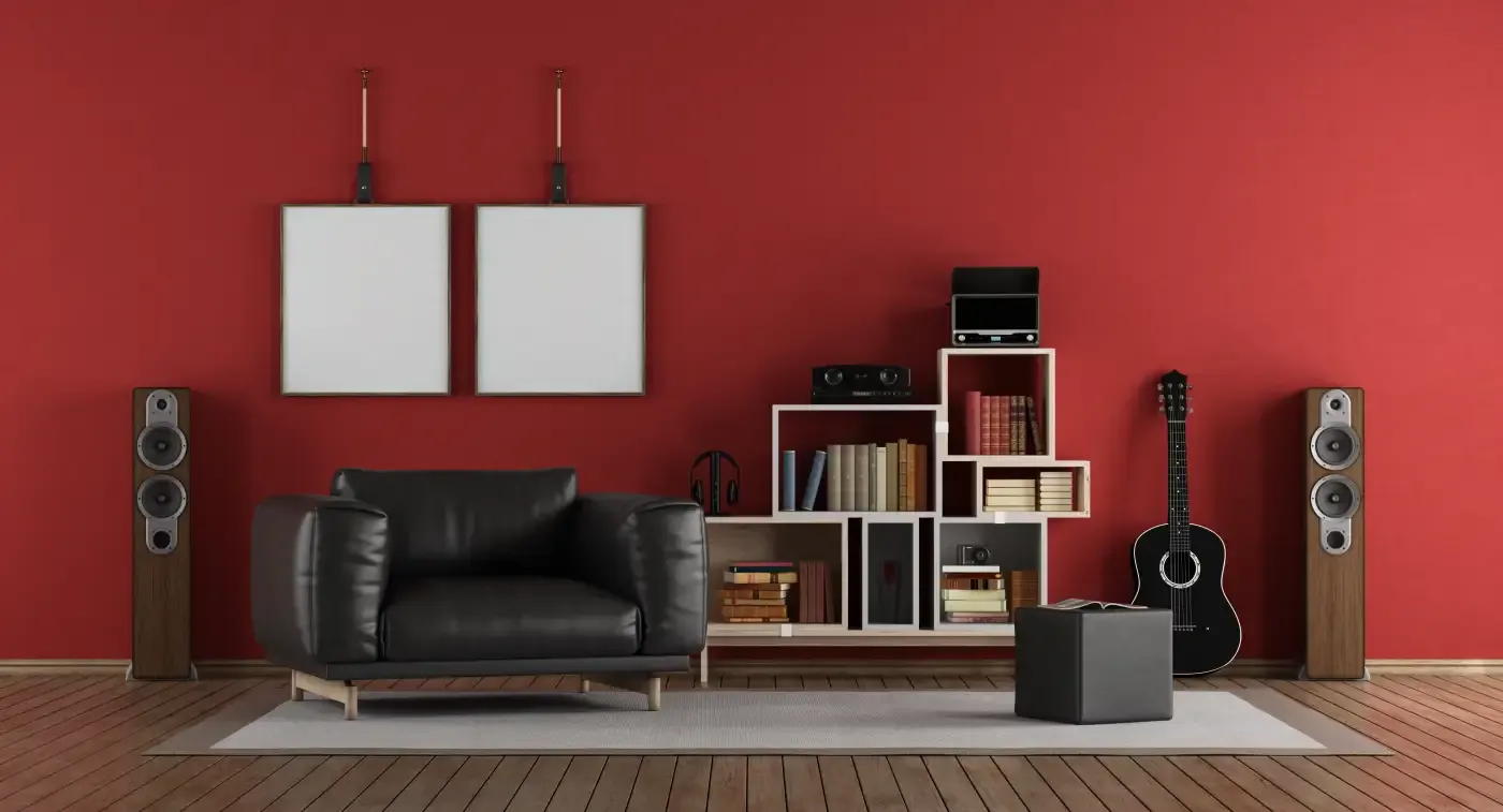 A cozy living room with a black leather armchair, wooden speakers, and a guitar against a red wall. A white shelf holds books and audio equipment, creating a modern vibe.