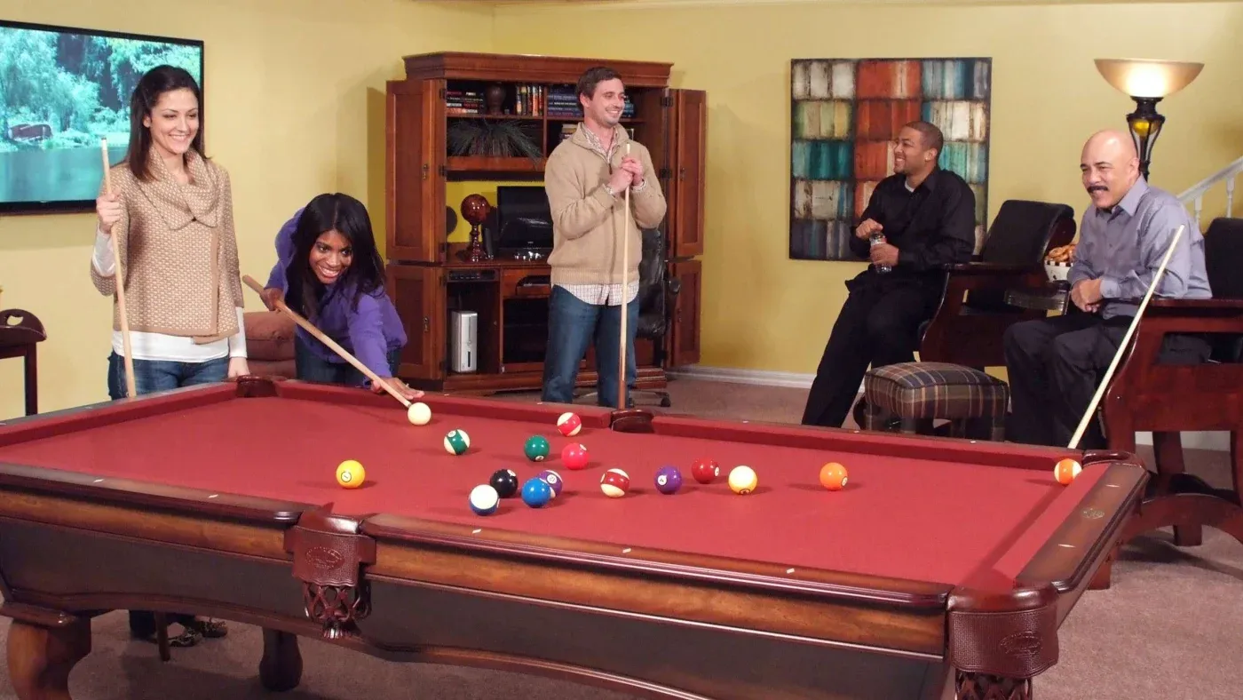 Four people enjoying a lively game of pool in a cozy living room. They are smiling and laughing, creating a cheerful and relaxed atmosphere.