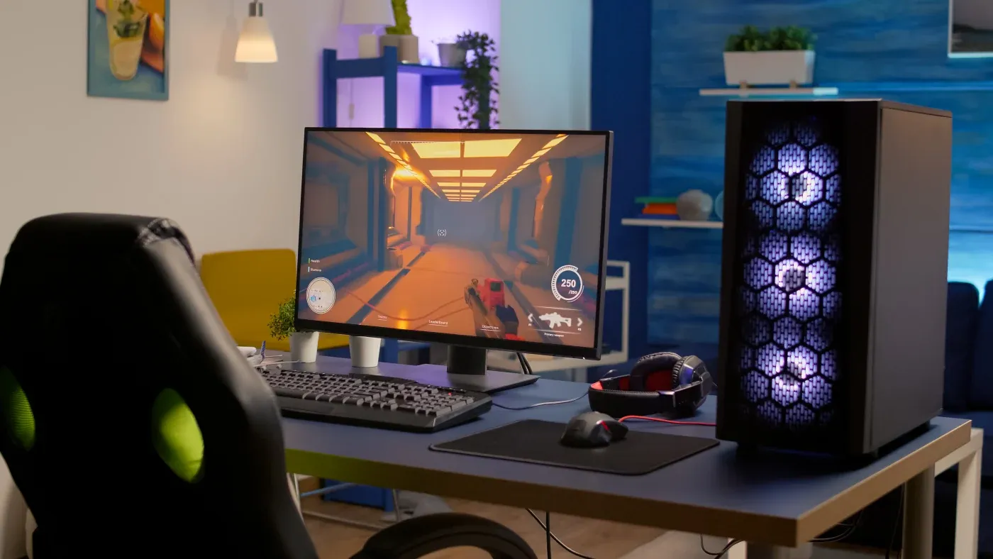 A gaming setup with a headset and a glowing tower beside a monitor showing a futuristic game. A modern room interior provides a cozy ambiance.