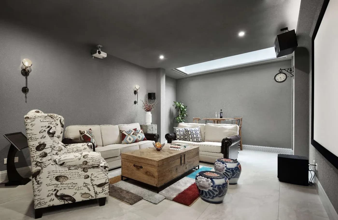 Stylish home theater room with cozy beige sofas, printed armchair, wooden coffee table, and large screen. Modern decor and a relaxed ambiance.