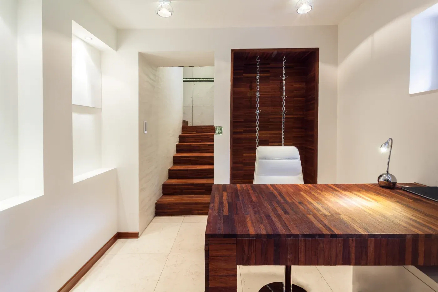 Modern office with wooden desk and suspended chair. Minimalist design, bright lighting, and white walls create a clean, contemporary atmosphere.