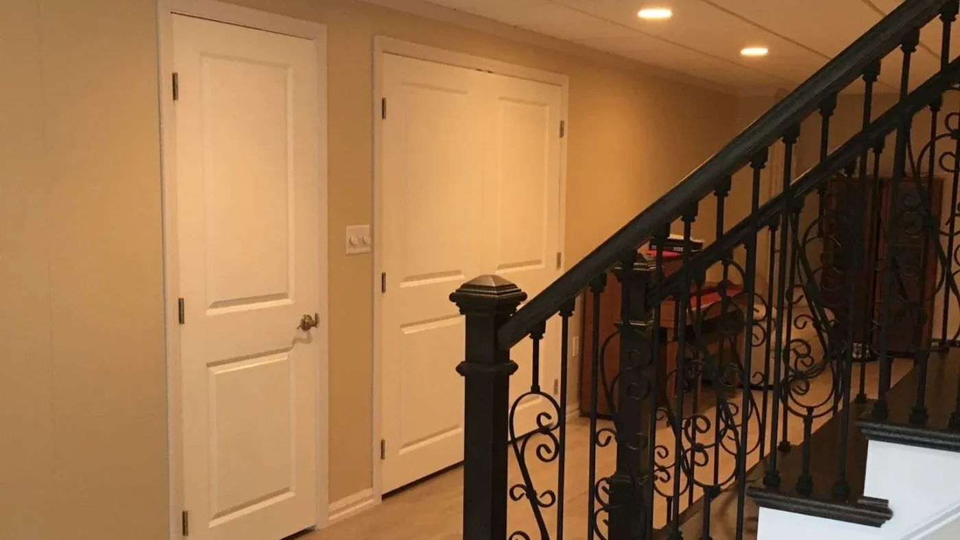 A warm-toned hallway features two white doors on the left and a decorative black wrought-iron staircase rail on the right, creating an inviting, elegant atmosphere.