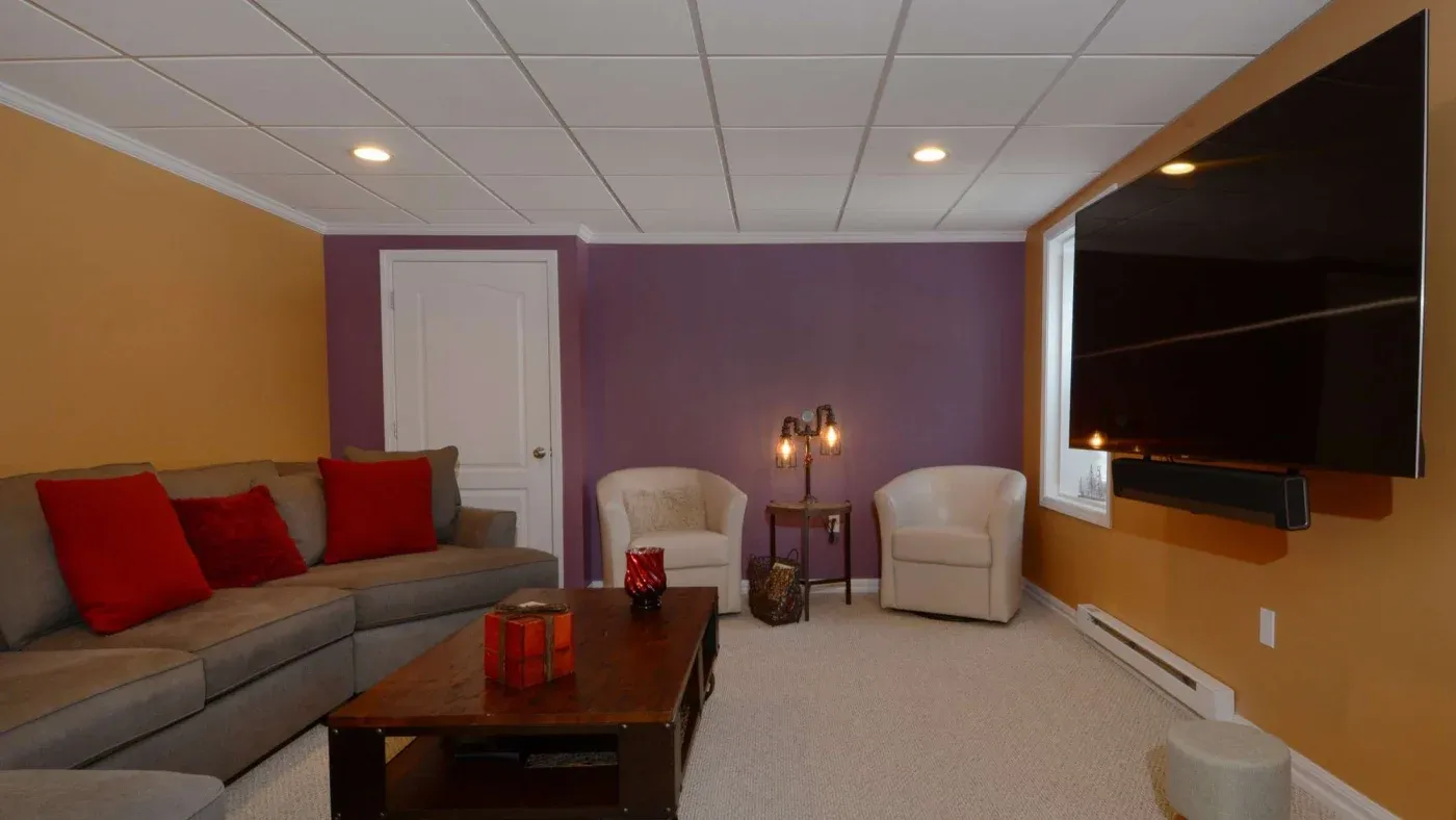 Cozy living room with a gray sectional sofa, red cushions, and a wooden coffee table. Two armchairs and a large TV create a warm, inviting atmosphere.