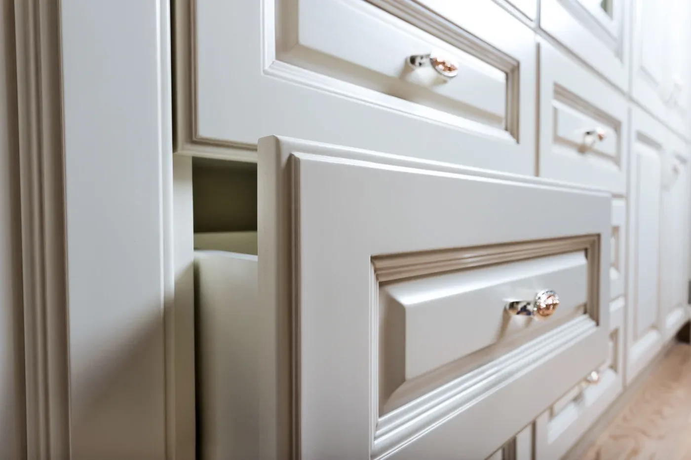 Close-up of an elegant white kitchen drawer, partially open, with shiny silver handles. The smooth, detailed woodwork conveys a sense of modern luxury.