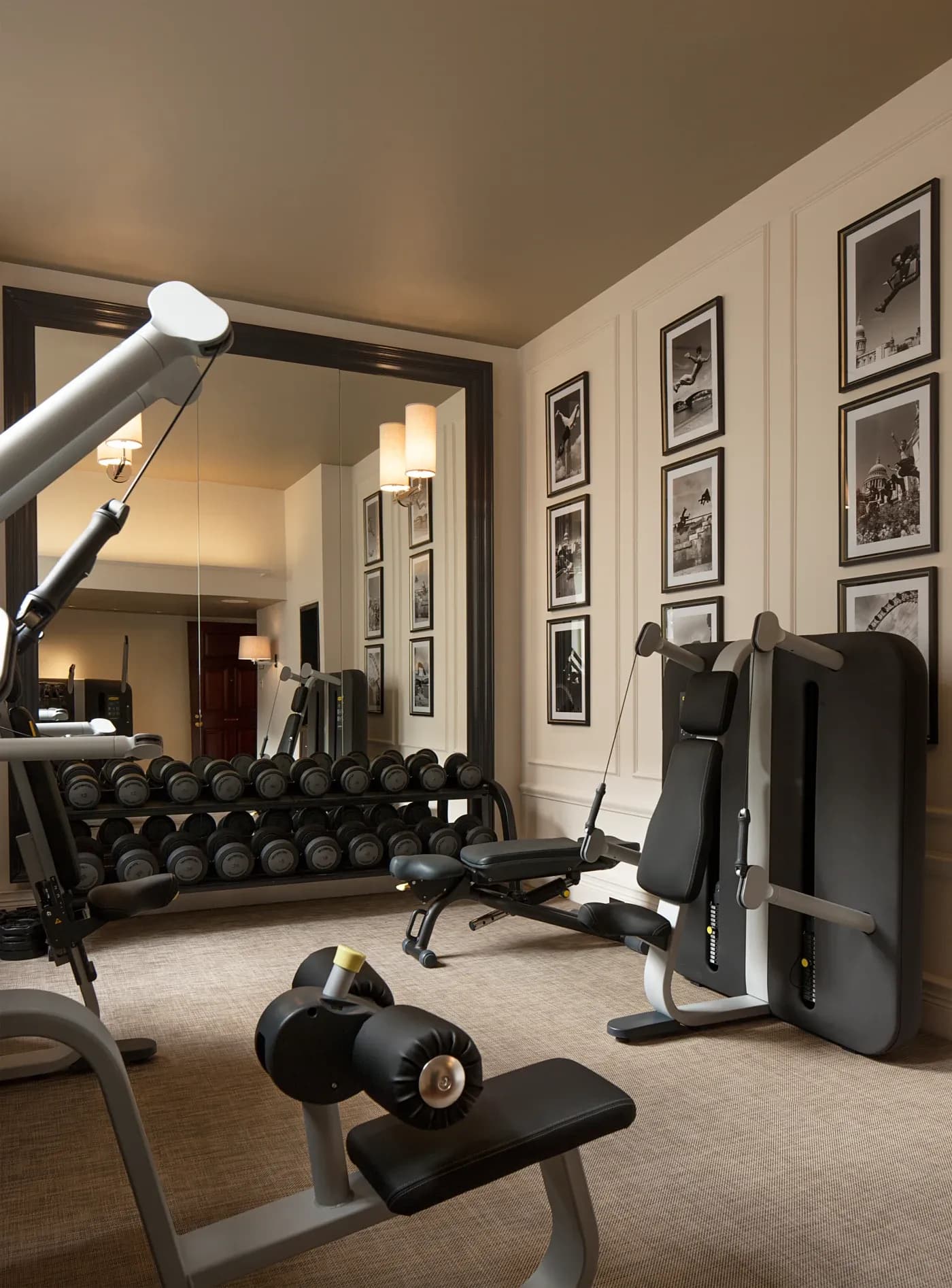 A modern home gym with exercise machines, a rack of dumbbells, and framed black-and-white photos on the wall. The room feels sleek and organized.