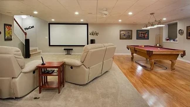 A cozy basement with a home theater setup featuring large recliners, a big screen, a pool table, and soft lighting, creating a relaxing, social atmosphere.