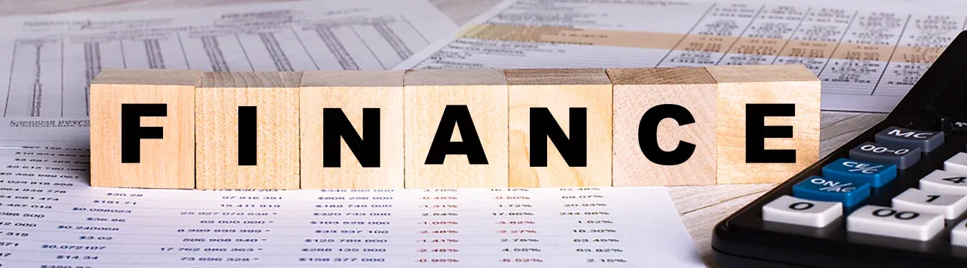 Wooden blocks spell "FINANCE" on financial documents. Nearby, a calculator suggests an analytical and professional tone.