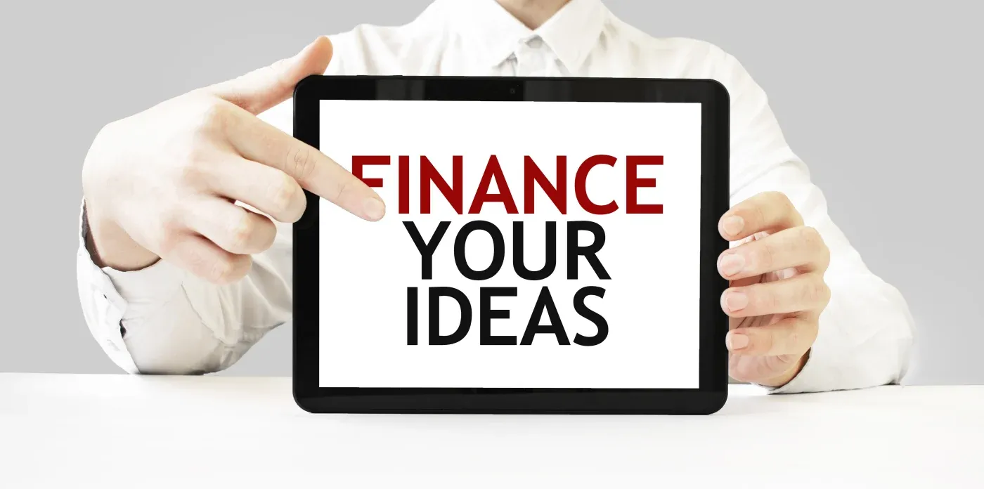 A person in a white shirt holds a tablet displaying the words "Finance Your Ideas" in bold red and black text, suggesting support for business innovation.