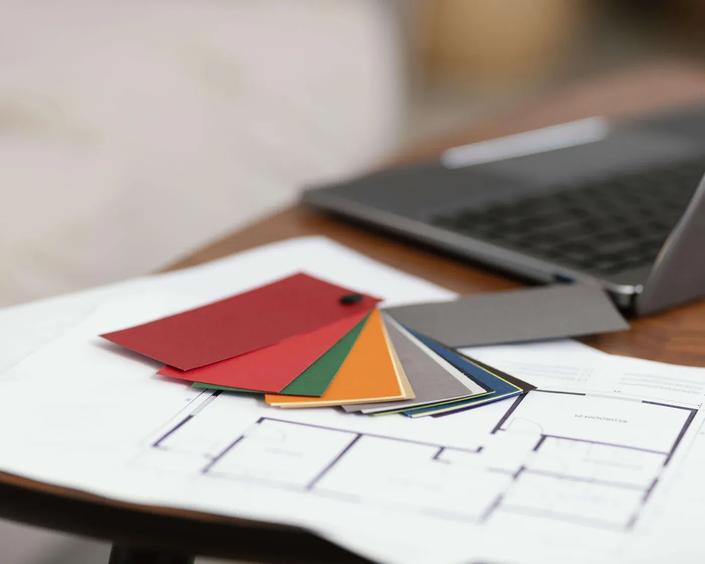 Color swatches and architectural plans rest on a table beside an open laptop. The setting suggests a design or architectural workspace.