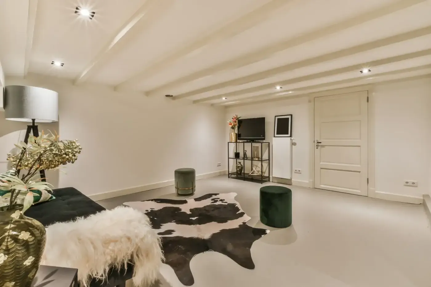 Stylish living room with a black sofa, white fur throw, cowhide rug, green pouffe, and TV on a stand. Warm lighting and minimalistic decor create a cozy atmosphere.