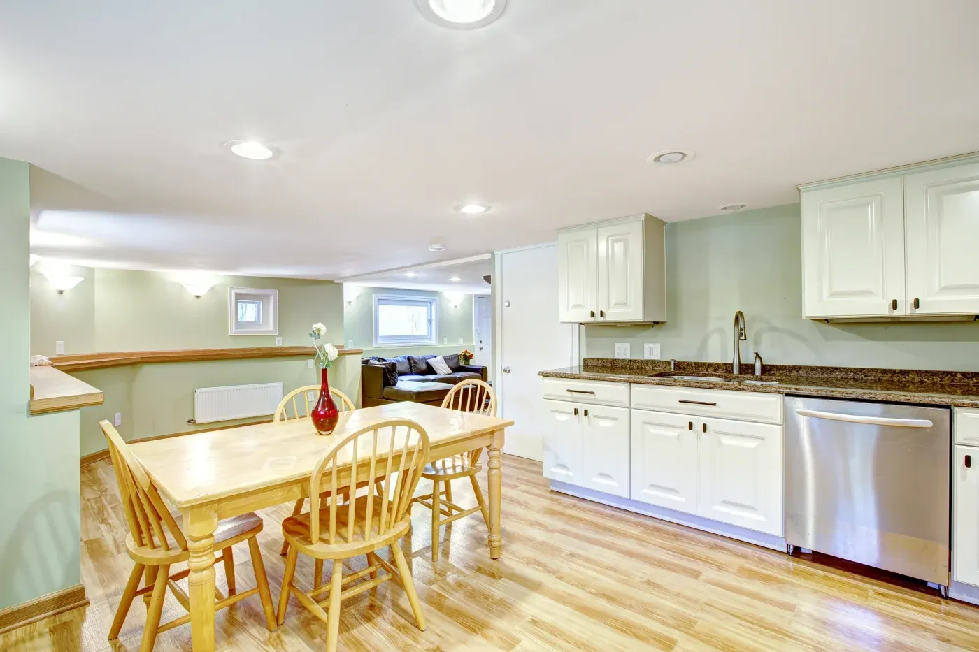 Bright kitchen with light wood flooring, featuring a wooden dining table and chairs. White cabinetry and stainless steel appliances exude a modern, cozy vibe.
