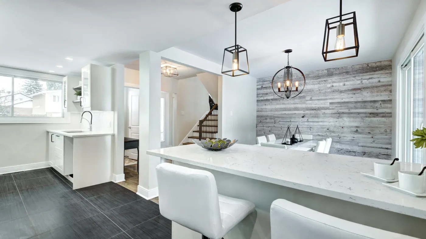 Modern kitchen and dining area with white countertops, sleek black tile flooring, and wooden accent walls. Pendant lights add an elegant touch.
