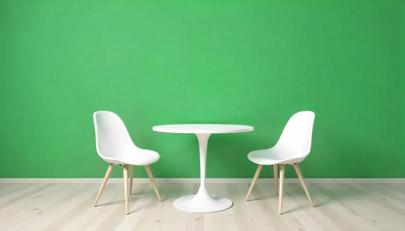 Two white chairs face each other across a round white table on light wood flooring, set against a bright green wall, conveying a minimalist style.