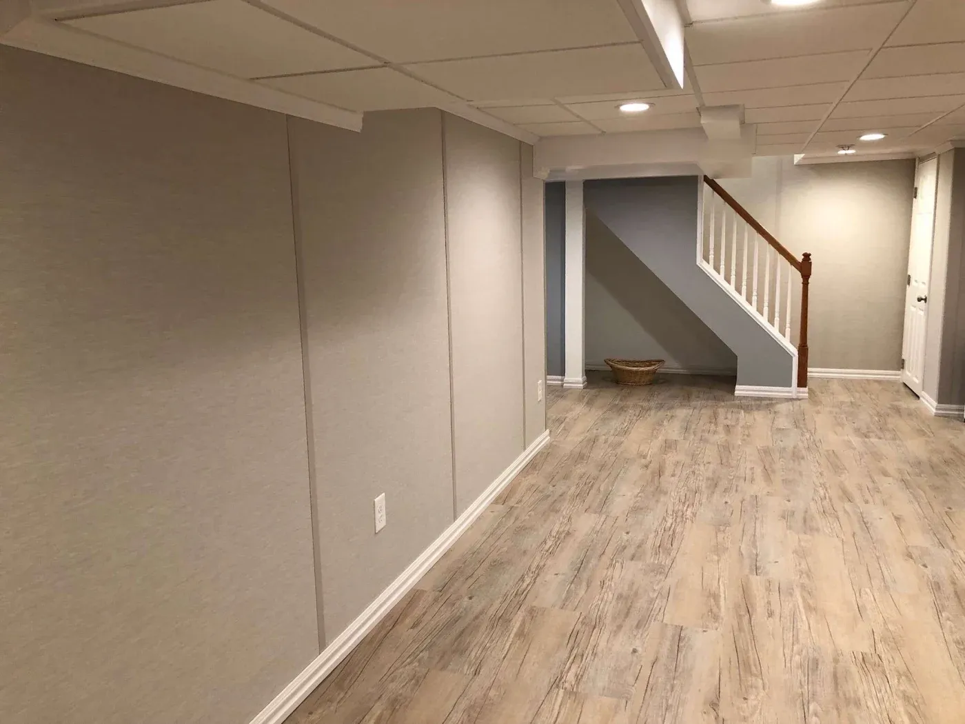 Finished basement with wood-look flooring, drywall partitions, recessed lighting, staircase with wooden handrail, and open floor plan