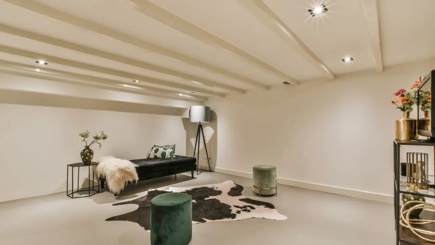 Stylish basement lounge with a modern black sofa, cowhide rug, velvet ottomans, standing lamp, and decorative shelves, conveying a cozy, elegant vibe.