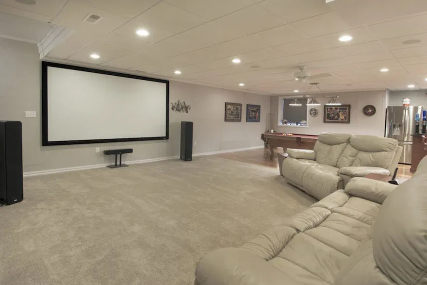 Spacious basement home theater with a large screen, surround sound speakers, and plush recliners. In the background, a pool table adds a fun element.