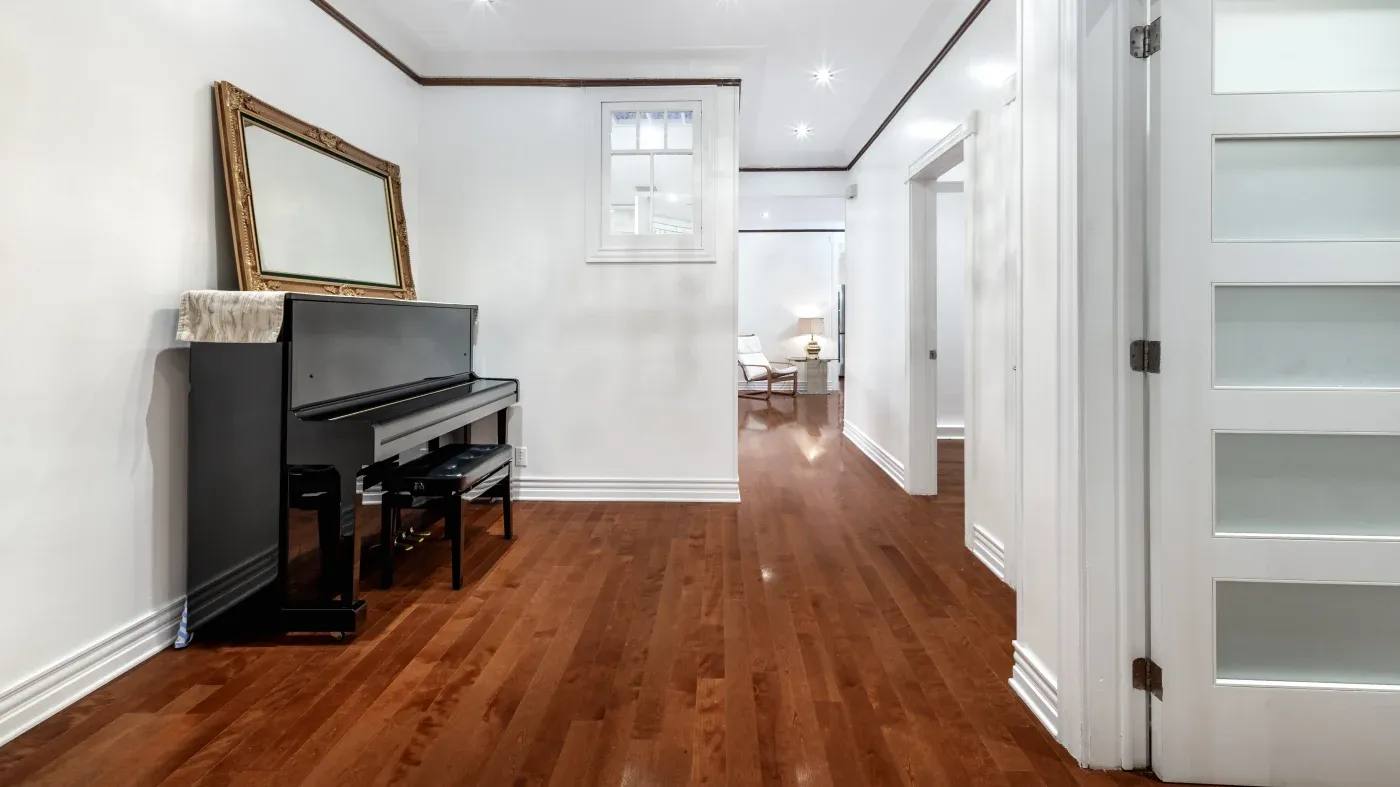 Spacious, well-lit hallway with polished wooden floor, featuring a black upright piano and ornate mirror. Modern, minimal decor conveys elegance.