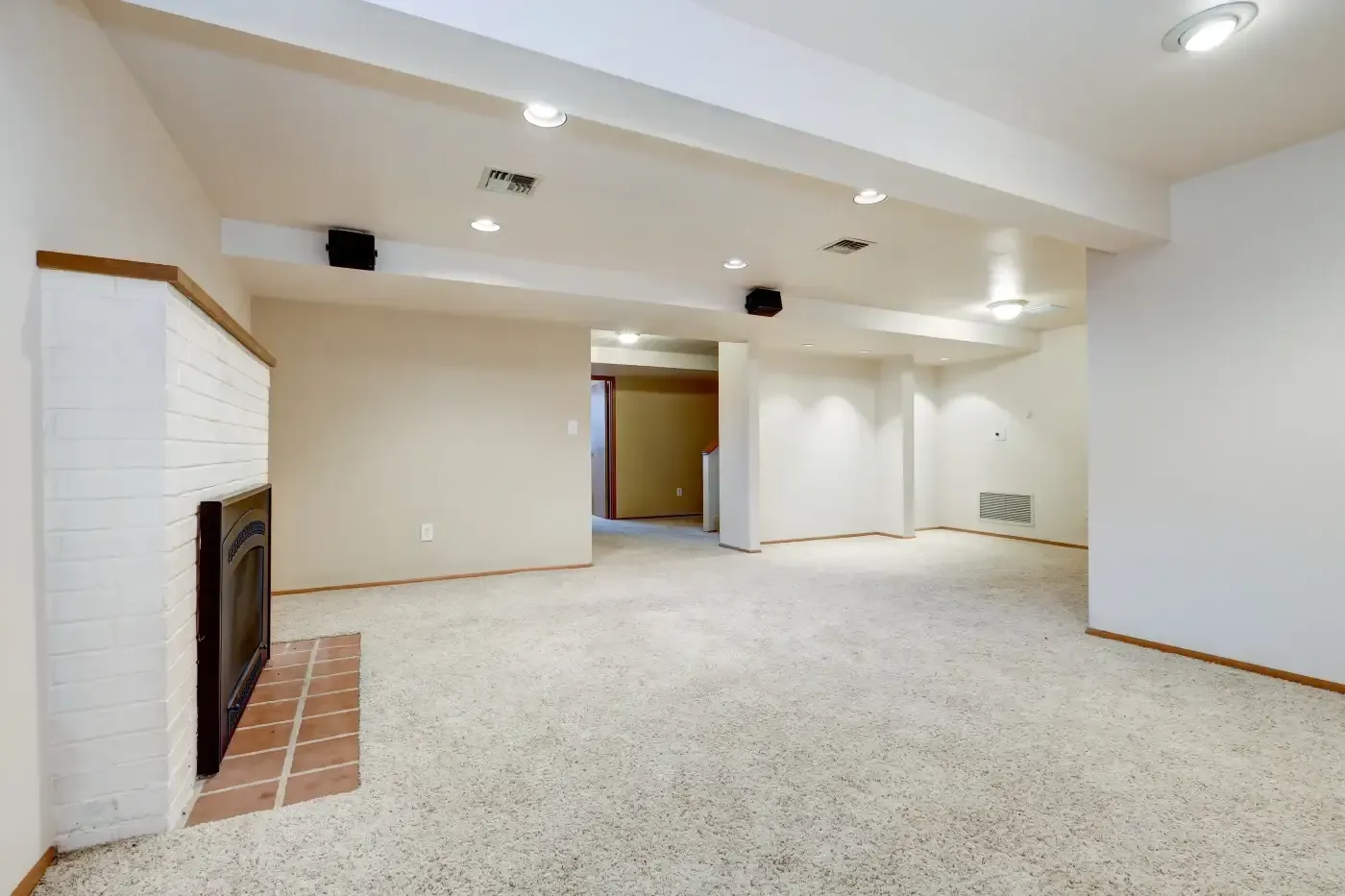 Spacious basement with beige carpet, white walls, and a white brick fireplace. Recessed lighting creates a warm atmosphere. Open space suggests potential for various uses.