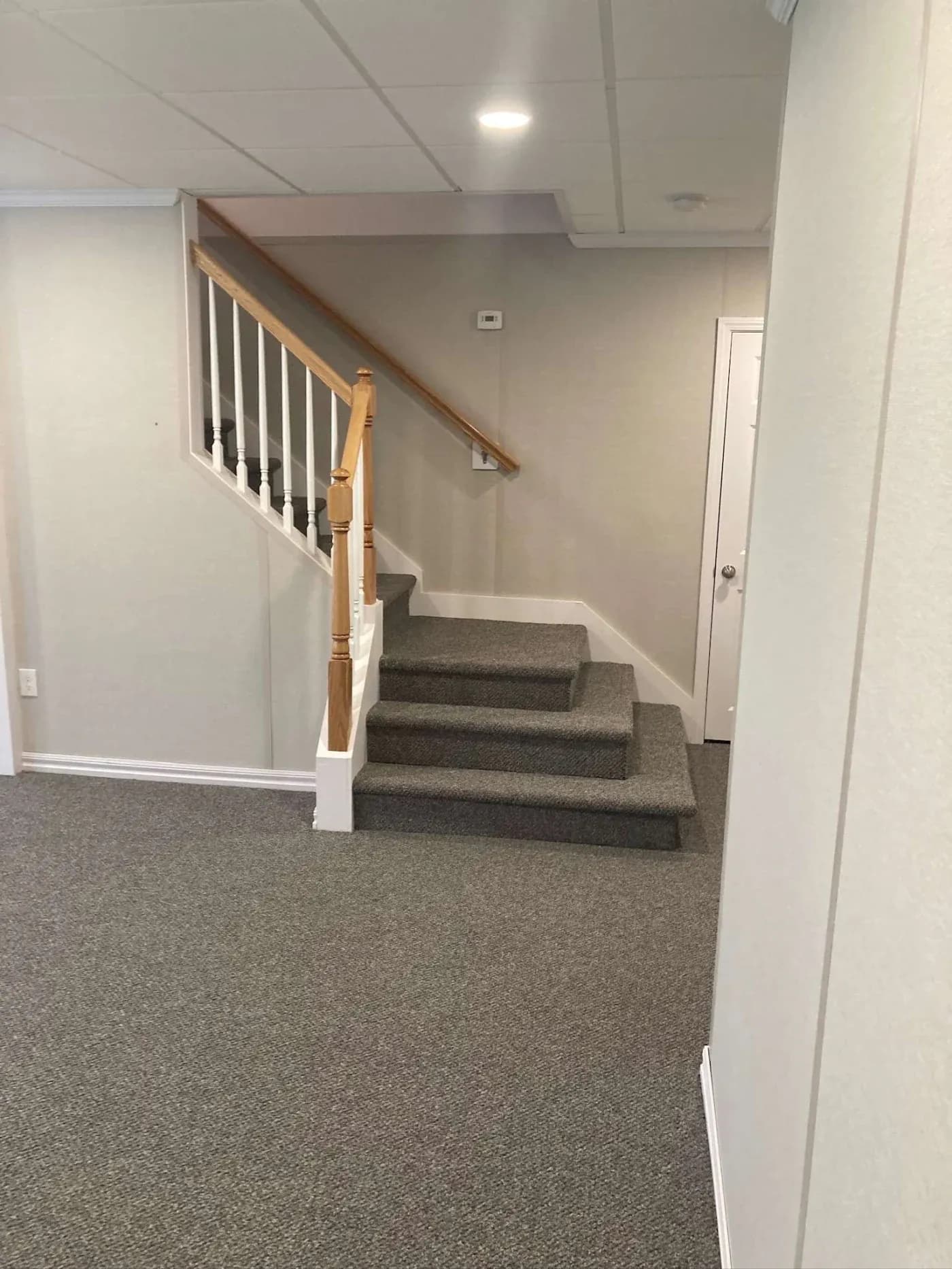 A carpeted staircase with a wooden handrail leads to a small hallway. Neutral-colored walls and ceiling lights create a clean, modern feel.