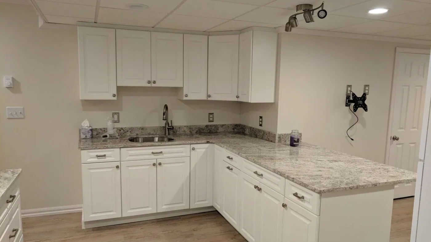 A modern kitchen with white cabinetry, granite countertops, and a small sink. Soft lighting enhances the clean, minimalist look and cozy atmosphere.