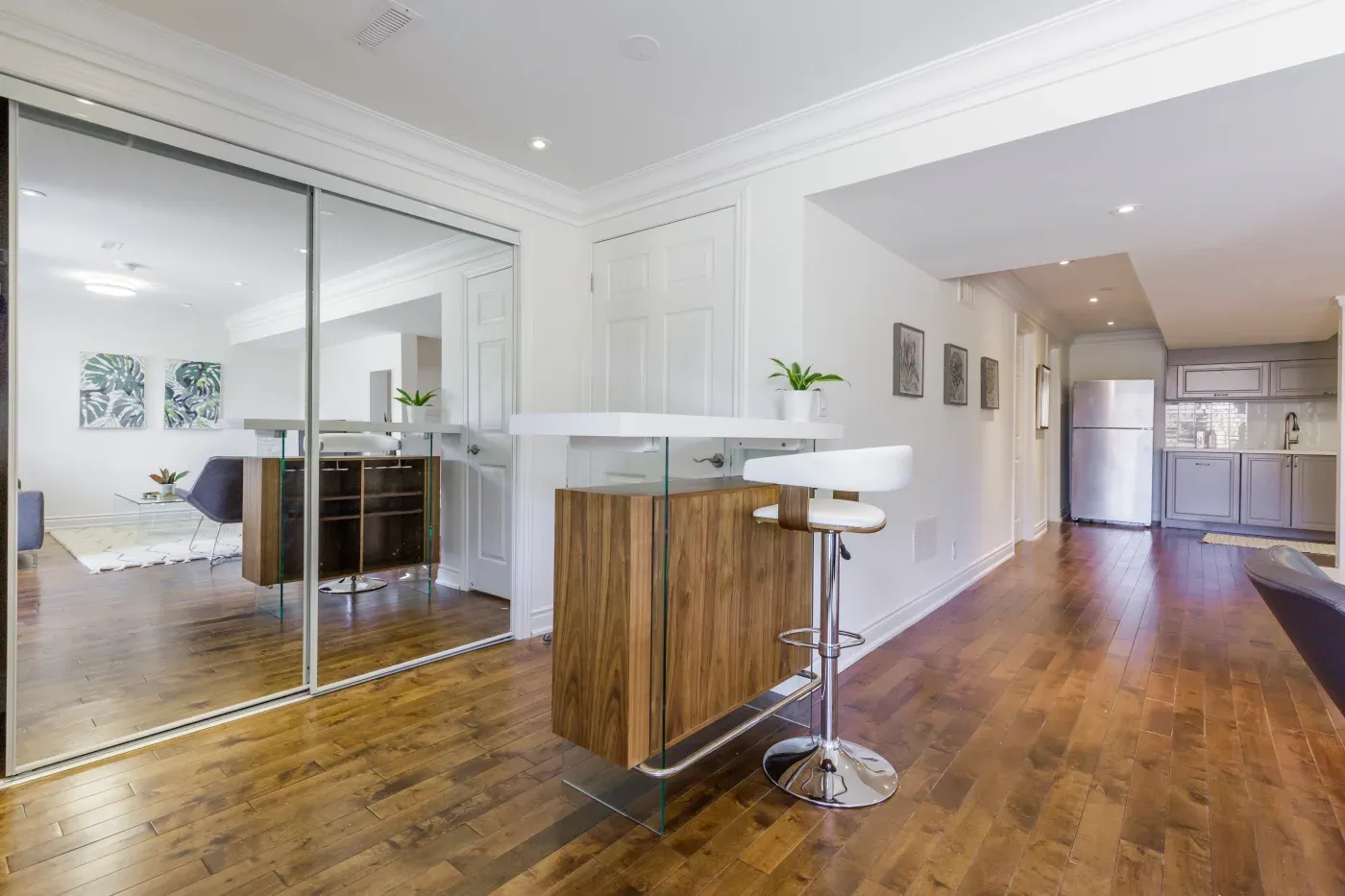 Modern kitchen with wooden floors, a mirrored wall, and a sleek bar area with stools. Bright, airy, and minimalist with soft, natural lighting.
