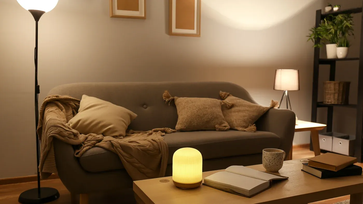 Cozy living room with a gray sofa adorned with beige pillows and a blanket. Soft lighting from lamps creates a warm, inviting atmosphere.