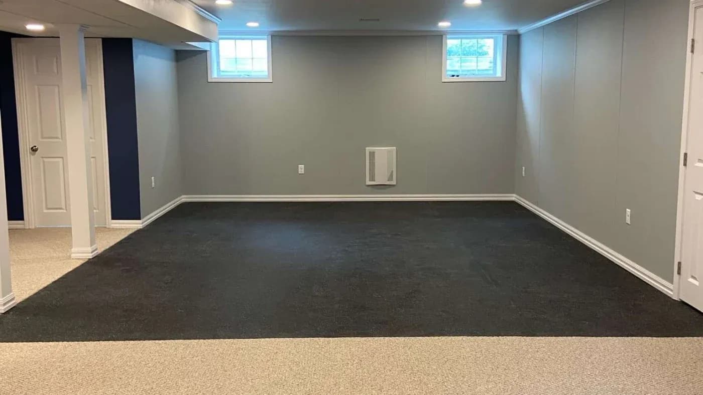 Finished basement with two small windows, gray walls, and recessed lighting. Features a mix of dark and light carpeting, creating a modern, spacious feel.