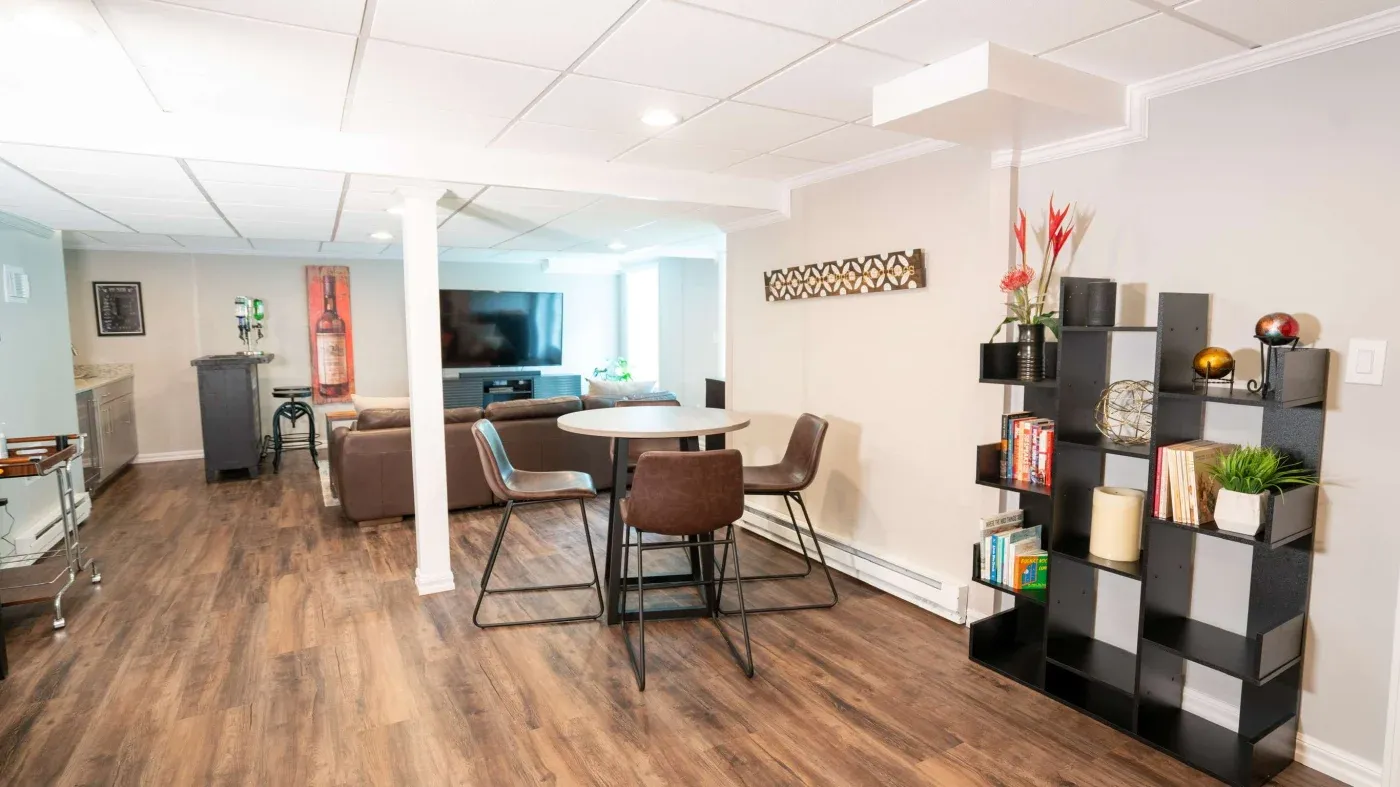 Modern living space with hardwood flooring featuring a circular dining table and chairs, a bookshelf, and a TV area with comfortable seating. Bright and inviting.